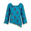 A turquoise blue long-sleeve top with a square neckline, decorated with colorful paisley-like motifs and a gold tassel fringe along the hem and cuffs, shown against a plain white background.