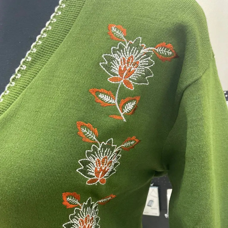 Green sweater with floral embroidery on a blurred background