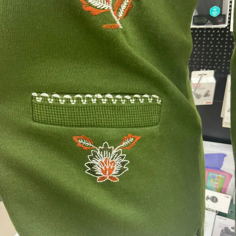 Green fabric with orange floral embroidery on a display stand.